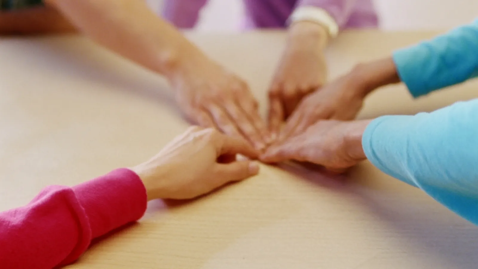 Hands from several people meeting at the center of a wooden table