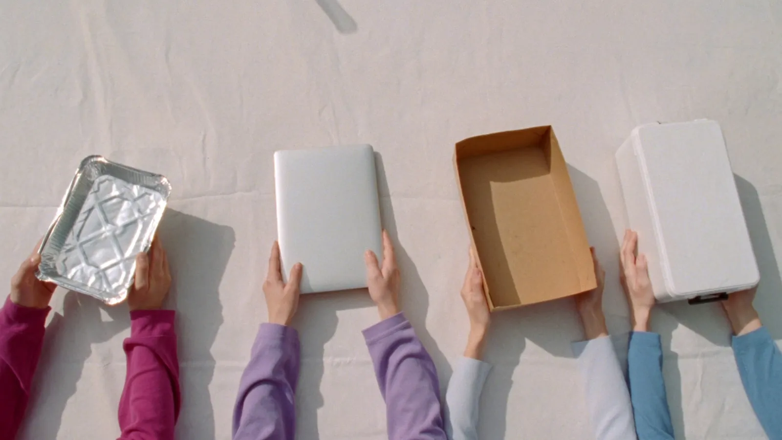 Four pairs of hands holding a meal tray, a laptop, a food box, and a medical supply case